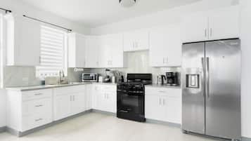 Cozinha moderna com armários brancos, eletrodomésticos de aço inoxidável e fogão preto.