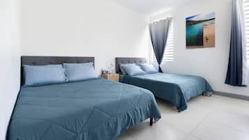 A bedroom with two beds, a nightstand, a window with curtains, and a wall-mounted picture.