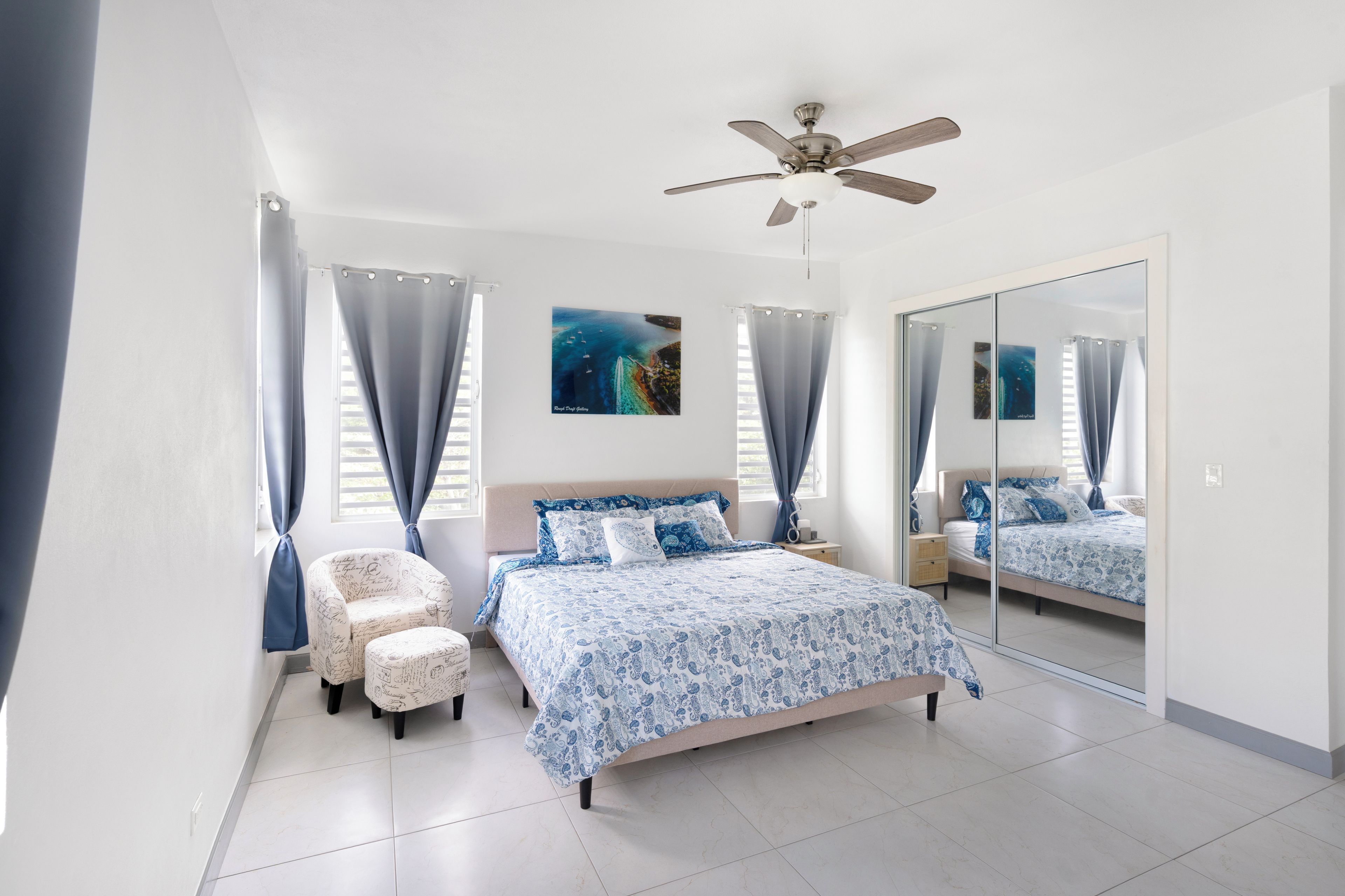 A bedroom with a bed, a chair, a ceiling fan, and a large mirror.
