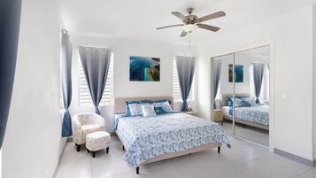 A bedroom with a bed, a chair, a ceiling fan, and a large mirror.