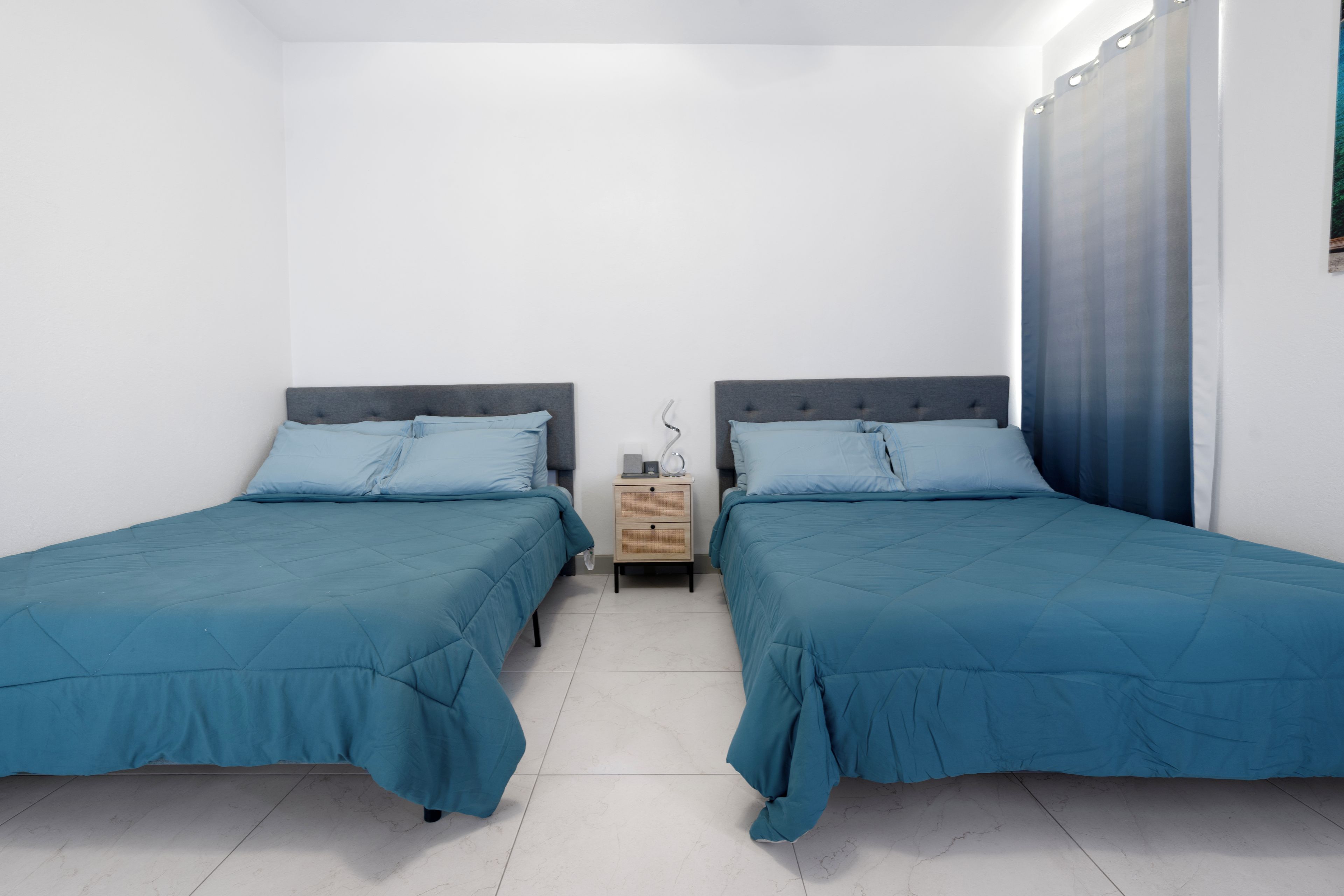 A twin room with two beds, a nightstand, and a window with curtains.