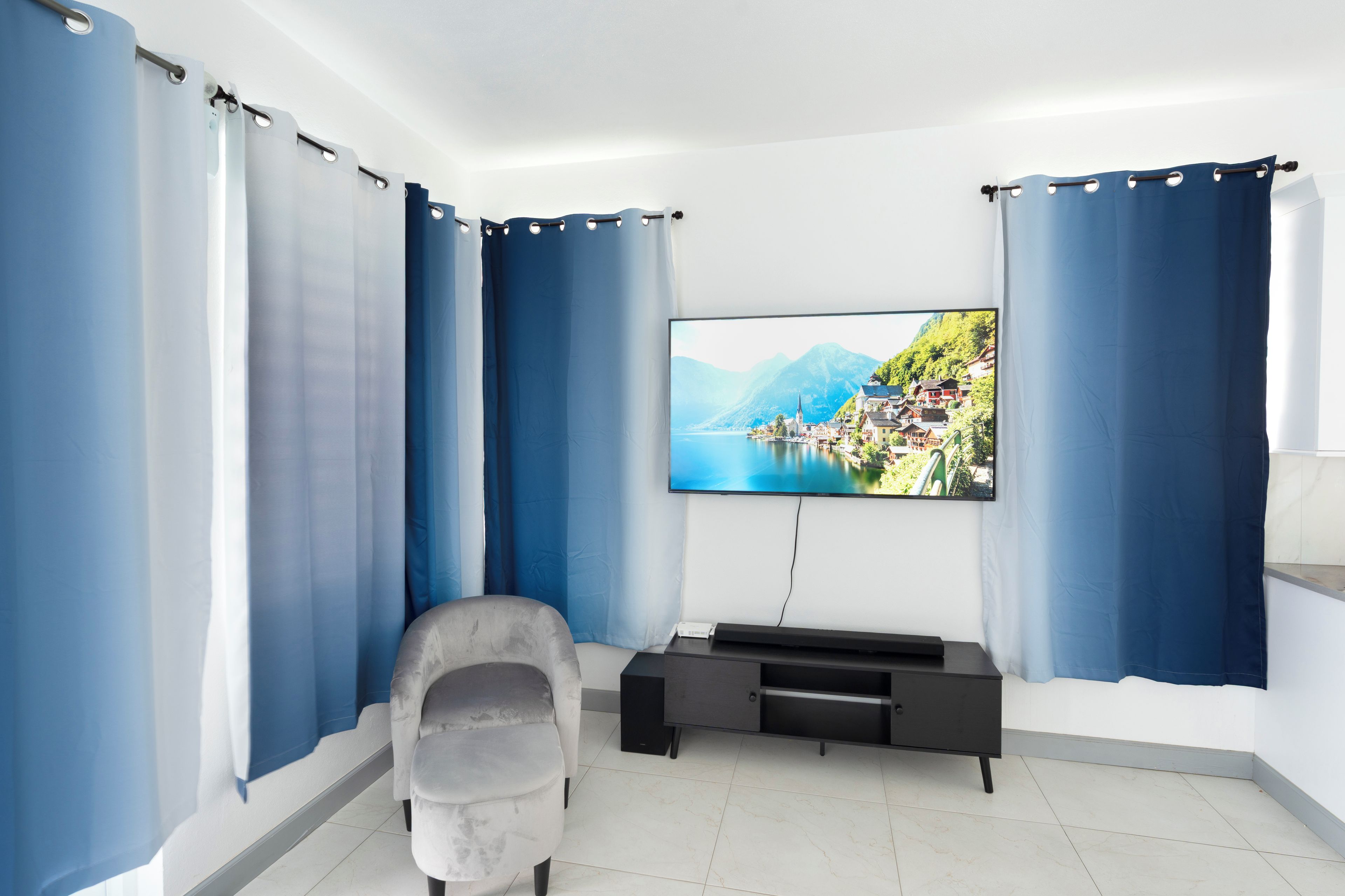 A modern living room with a flat-screen TV mounted on the wall, a grey sofa, and a black entertainment unit.