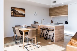 A modern kitchen with a wooden island, bar stools, and a dining table with chairs. - 3 x Townhouses • Central • Modern (Raglan)