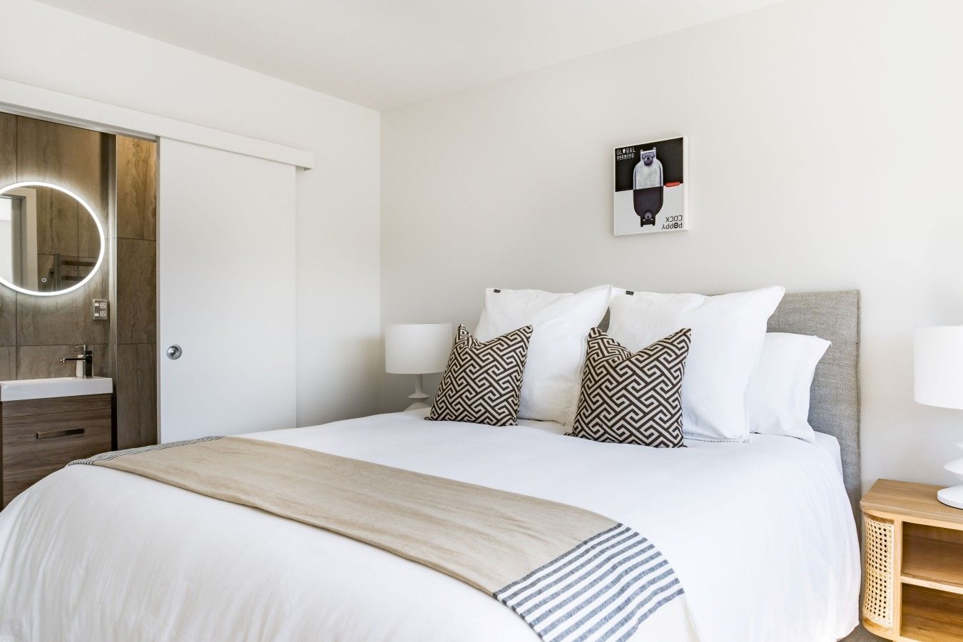 A hotel room with a bed, bedside lamps, a wooden door, a mirror, and a wall-mounted artwork.