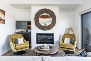 A modern living room with two armchairs, a fireplace, a round mirror, and a television. - 3 x Townhouses • Central • Modern (Raglan)