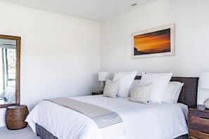 Ein Schlafzimmer mit einem großen Bett, Nachttischlampen, einem Spiegel und einem Sonnenuntergangsbild an der Wand.