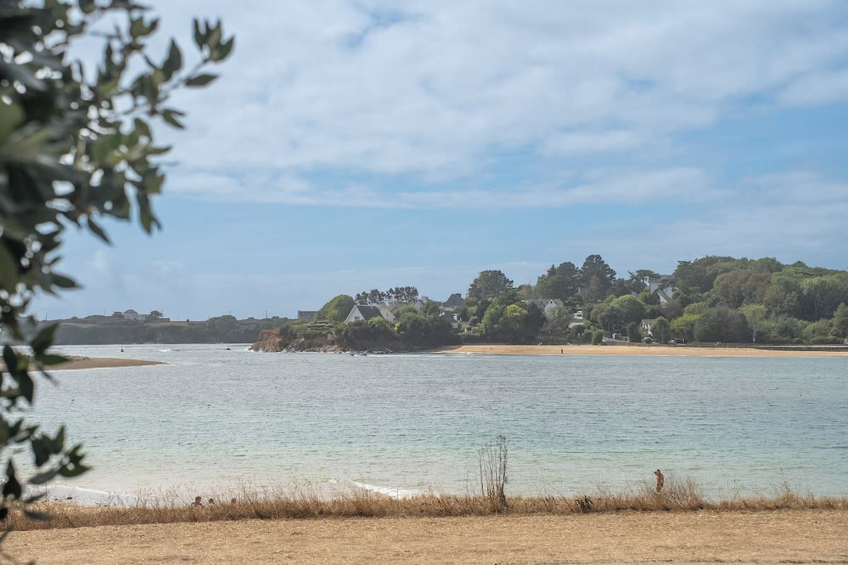 Un paisaje costero con una masa de agua, una playa de arena y un conjunto de edificios en una colina.