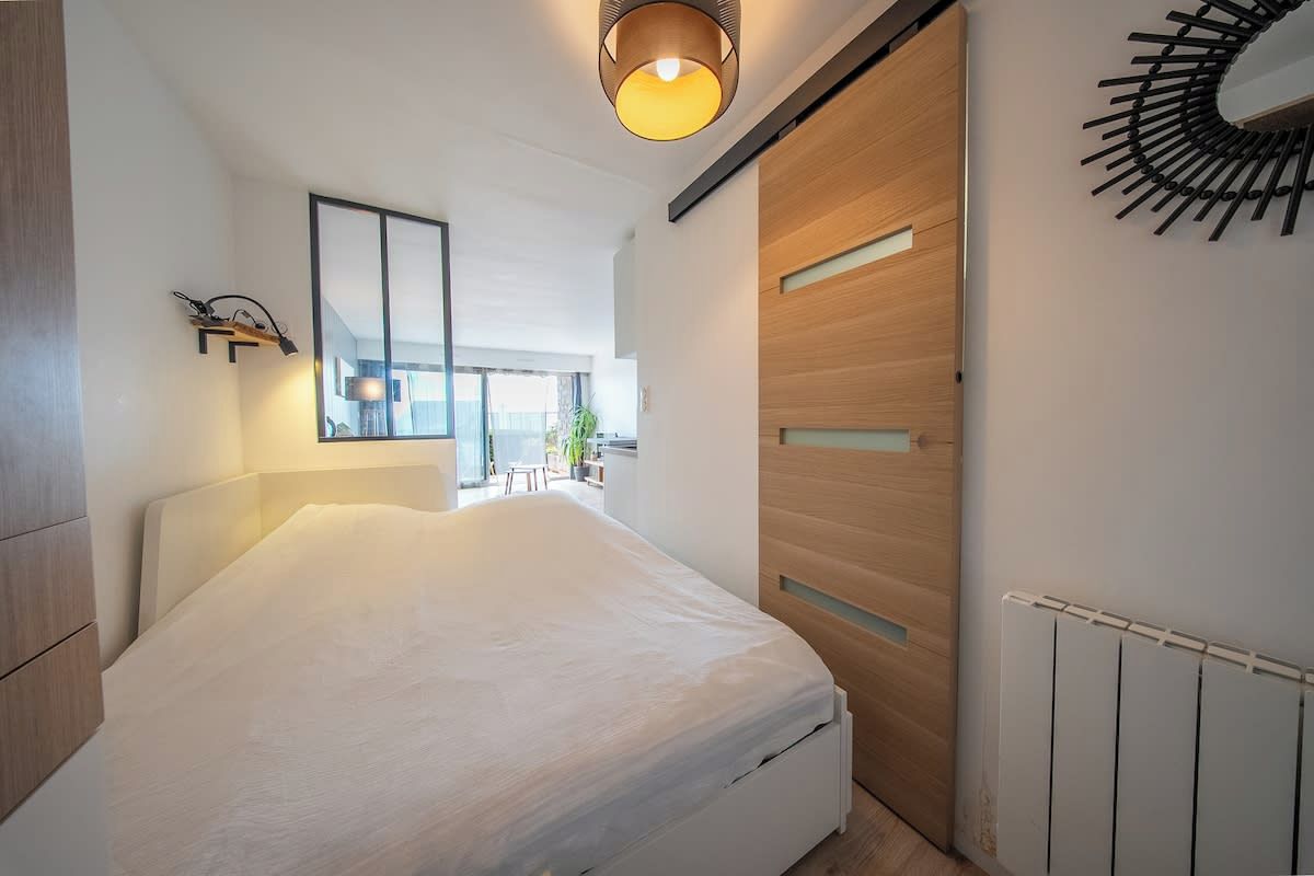 A modern bedroom with a bed, a wall-mounted mirror, a wooden wardrobe, and a radiator.