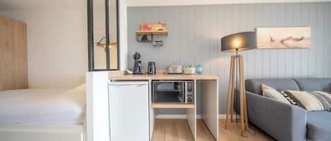 Habitación compacta con cama, kitchenette, escritorio, sofá y lámpara de pie.