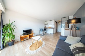 Ein modernes Wohnzimmer mit Flachbildfernseher, einer Couch, einem Essbereich und einer Küche im Hintergrund.