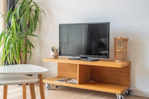 Ein Flachbildfernseher auf einem Holz-TV-Möbel mit Fernbedienung, einer kleinen Pflanze und einem dekorativen Korb.