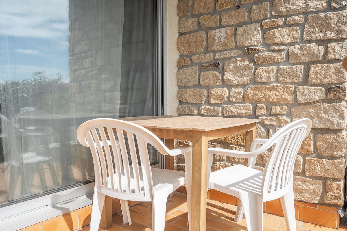 A wooden table and two white chairs positioned on a balcony with a stone wall backdrop.