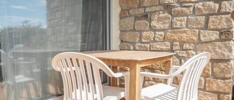 A wooden table and two white chairs positioned on a balcony with a stone wall backdrop.