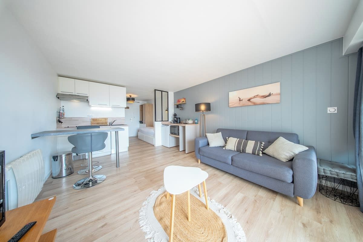 Un espace de vie moderne comprenant un canapé gris, une table à manger et un coin cuisine.