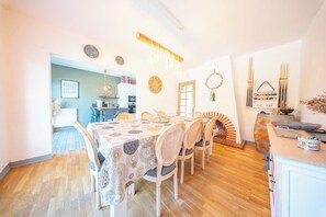 A dining area with a table set for six, surrounded by wicker chairs. A wooden barrel and a wall-mounted rack with paintbrushes are visible. - Maison de Famille Vue Mer - Port & Côte Sauvage (Quiberon)