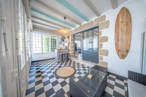 A room with a checkered floor, a glass table, and a surfboard on the wall. - Maison de Famille Vue Mer - Port & Côte Sauvage (Quiberon)