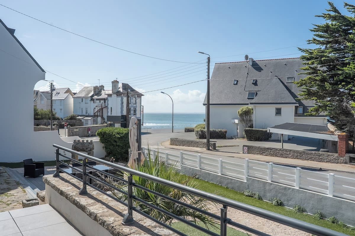 A coastal street with buildings, a white fence, and a clear view of the sea.