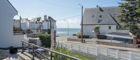 A coastal street with buildings, a white fence, and a clear view of the sea.