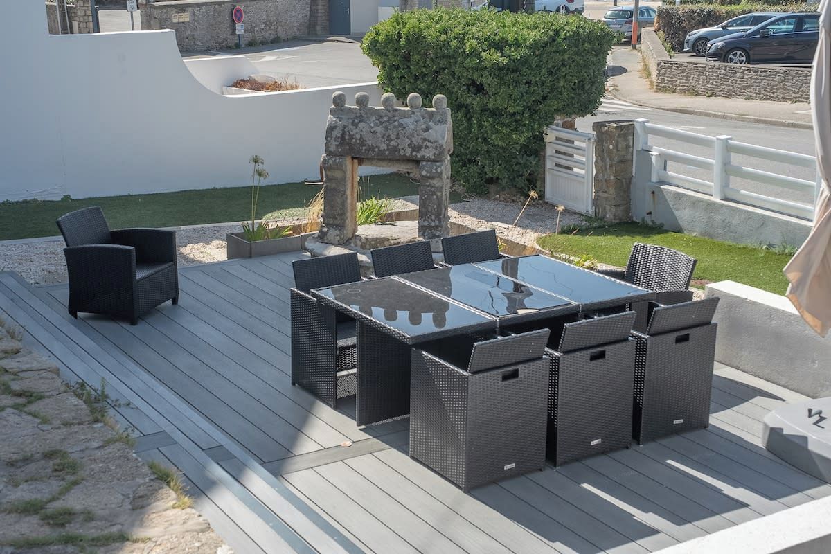 An outdoor patio with a dining table and chairs, surrounded by a white wall and a hedge.