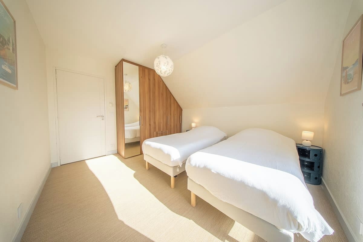 A bedroom with two beds, a wooden wardrobe, a mirror, a nightstand with a lamp, and a ceiling light fixture.