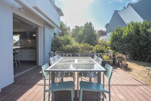 An outdoor patio with a table and chairs, surrounded by greenery and a house. - Ecrin de Douceur - Plages, Port & Confort (Ploemeur)