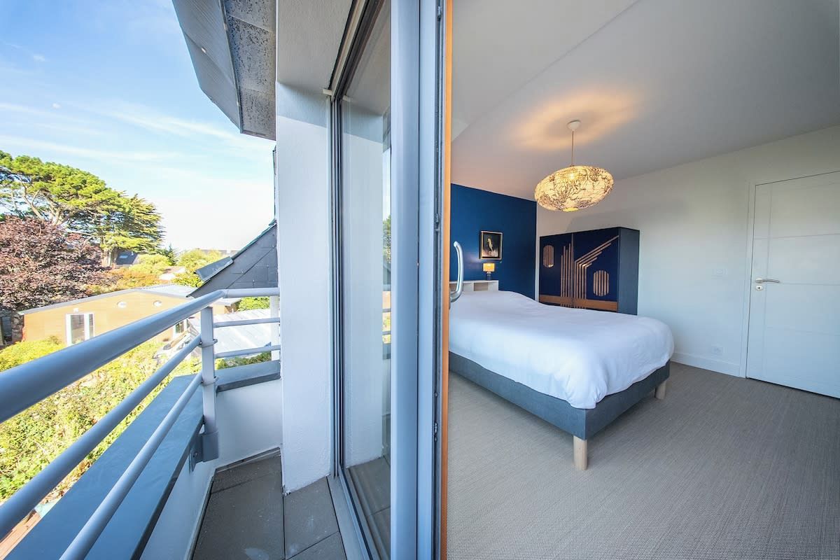 A bedroom with a bed, a door, and a view of the outdoors.