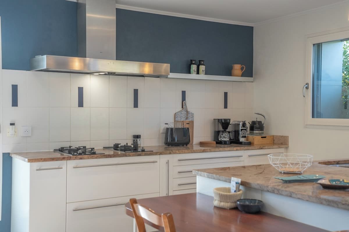 Une cuisine moderne avec des meubles blancs, une hotte en acier inoxydable et une machine à café.