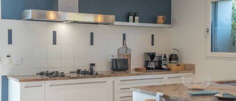A modern kitchen with white cabinets, a stainless steel range hood, and a coffee maker.