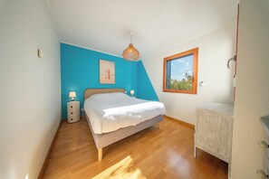 Ein Schlafzimmer mit einem Bett, Nachttischen, einer Hängelampe, einem Fenster und einer Tür.