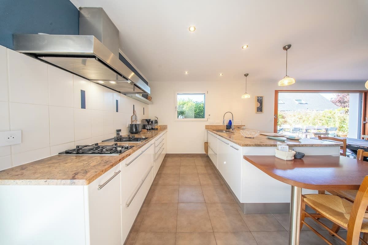 A modern kitchen with a gas stove, stainless steel range hood, and a window overlooking greenery.