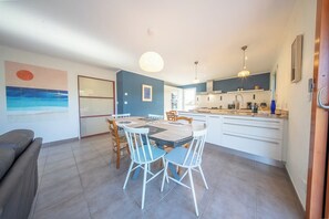 Eine moderne Küche mit weißen Schränken, ein Essbereich mit Tisch und Stühlen sowie ein Wohnzimmer mit einer Couch.