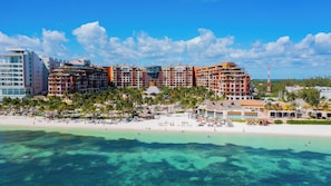 A beachfront hotel with multiple buildings, a sandy beach, and clear turquoise waters.
