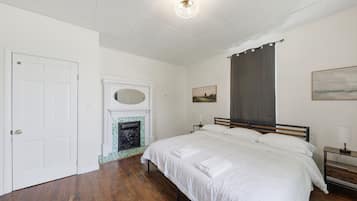 Un dormitorio con cama, mesita de noche, lámpara, cuadro, chimenea y puerta.