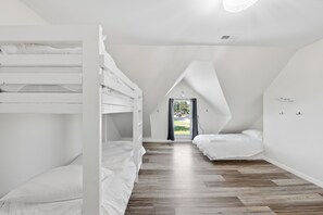A room with bunk beds, a sloped ceiling, and a view through a door.