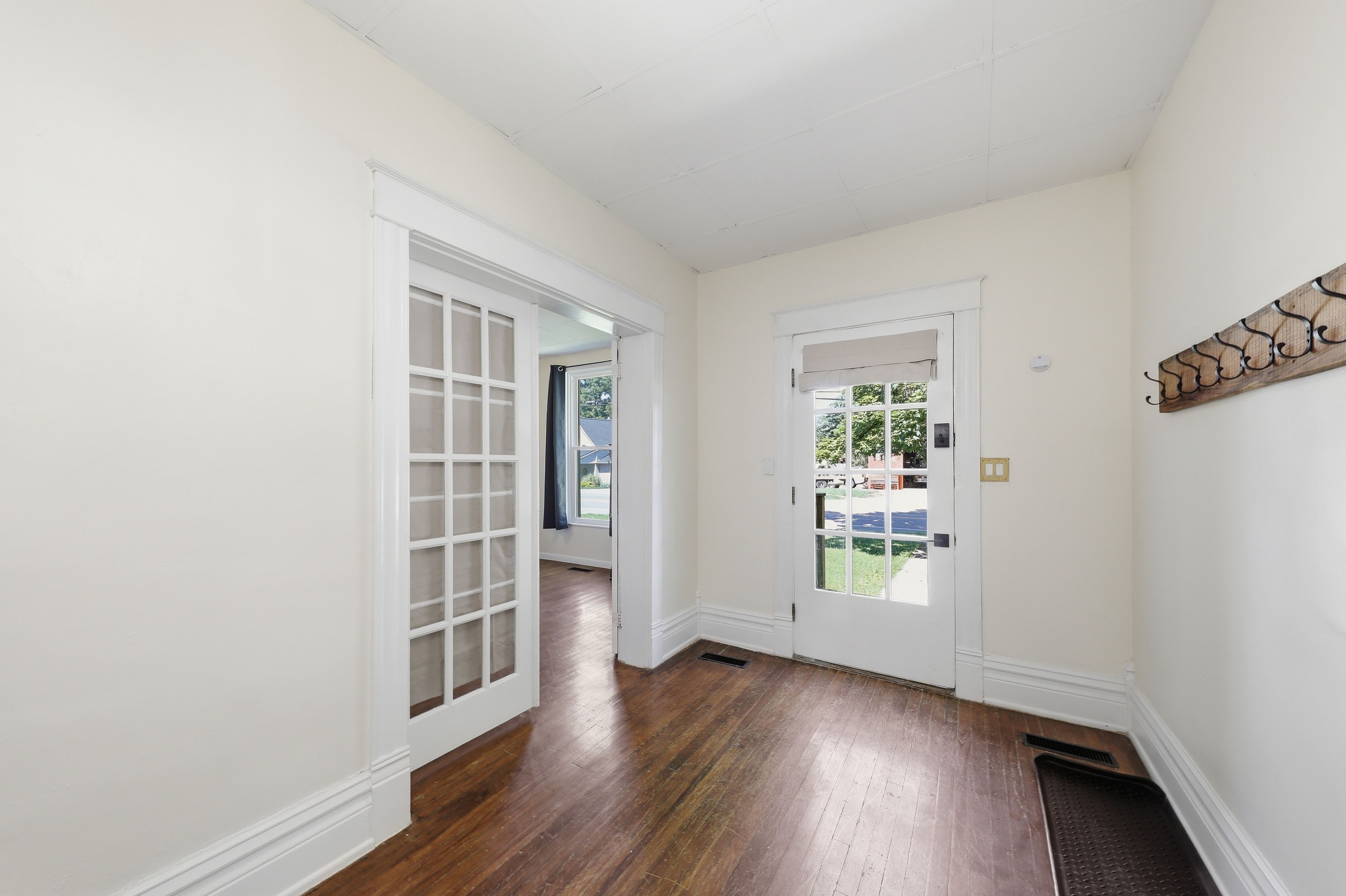 A hallway with white walls, wooden flooring, and a door leading to a backyard.