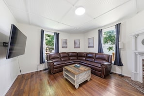 A living room with a brown leather sectional sofa, a wooden coffee table, and a flat-screen TV mounted on the wall.