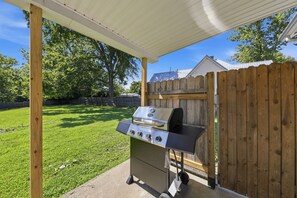 Een barbecue onder een overdekte patio met een houten hek op de achtergrond.