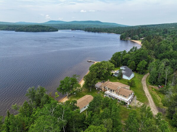 Une grande maison dotée d’un vaste porche, entourée d’une forêt dense et bordée d’un lac.