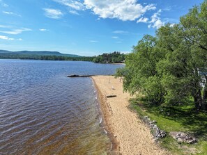 Une plage au bord d’un lac, avec une eau claire, un rivage sablonneux et une zone boisée.