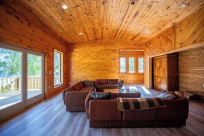A spacious wooden cabin interior with a large sectional sofa, a coffee table, and a fireplace. - The Chateaugay Lake Mansion (Lyon Mountain)