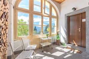 A room with a large arched window, a wooden door, and a small table with chairs. - Sunset View lago Maggiore (Maccagno Con Pino E Veddasca)