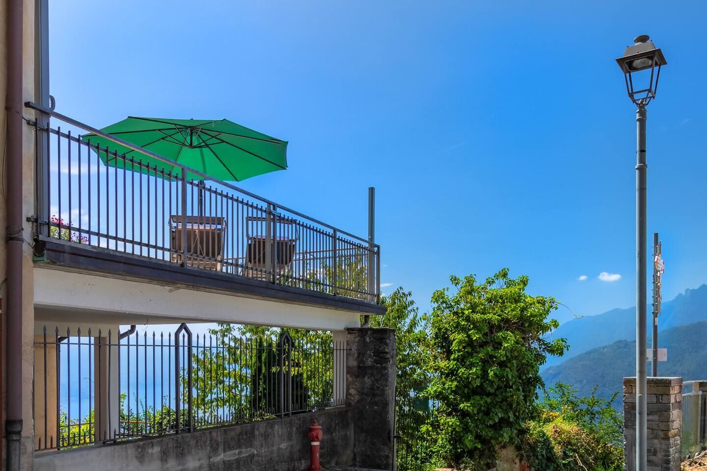Ein Balkon mit einem grünen Sonnenschirm, einem Hydranten und einer Straßenlaterne.