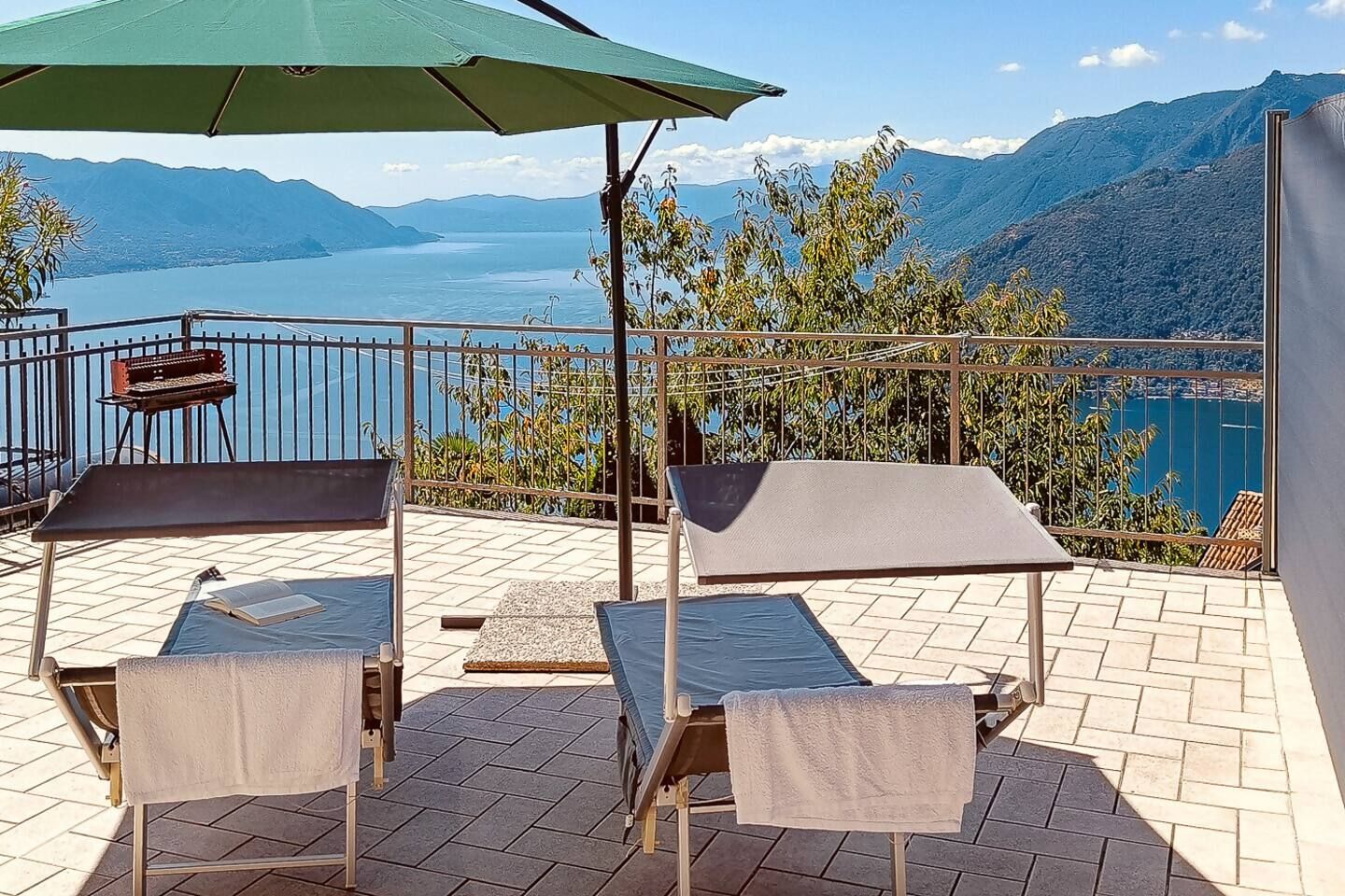 Una terraza con dos tumbonas, una parrilla y vistas a un lago y montañas.