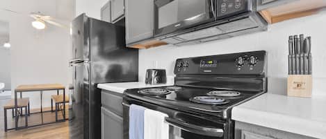 Una cocina moderna con un refrigerador negro, un microondas de acero inoxidable y una estufa negra. Hay una mesa de madera con sillas y un ventilador de techo.