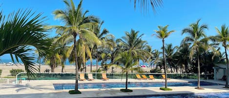 A pool area with palm trees, lounge chairs, and a view of the beach.