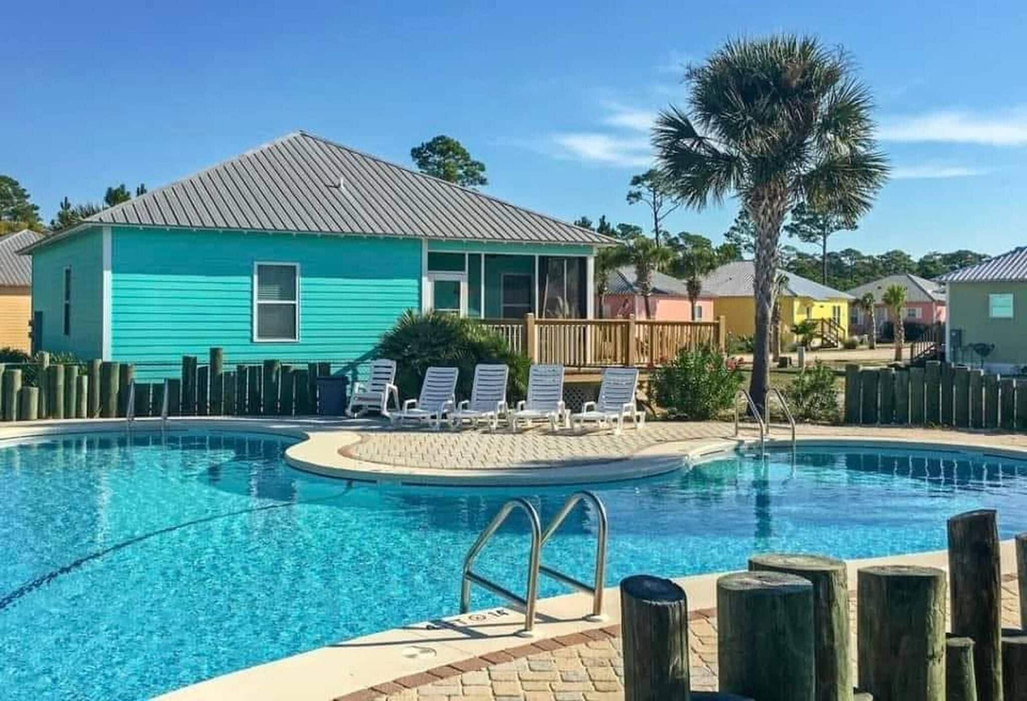 A swimming pool with lounge chairs, a wooden fence, and a turquoise building.