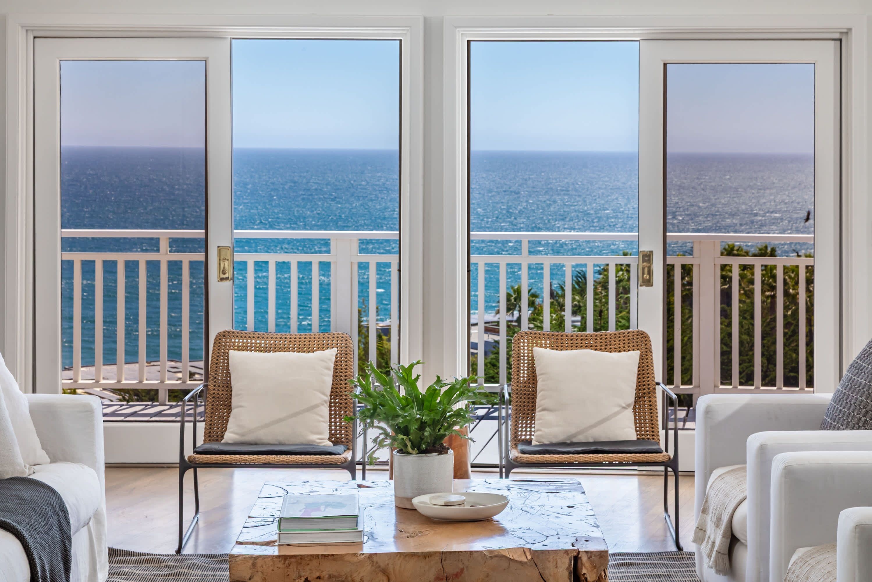 A balcony with a view of the ocean, furnished with wicker chairs and a coffee table.