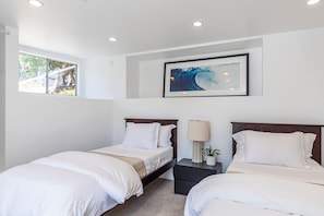 A hotel room with two beds, a window with a view of trees, a painting on the wall, and a nightstand with a lamp and a plant.