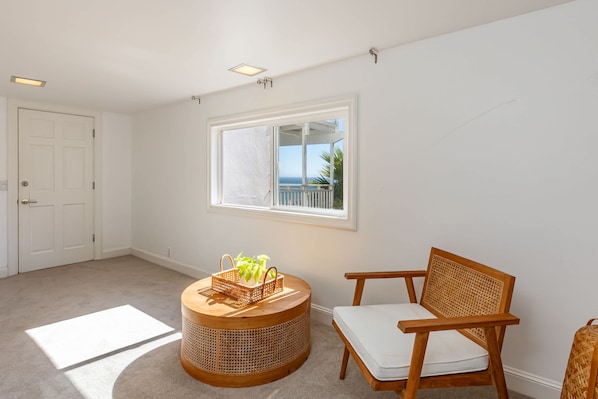 A room with a large window, a wicker basket with plants, a wooden chair, and a white door.