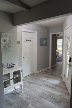 Un pasillo con una puerta blanca que dice 'Laundry', un mueble pequeño con un letrero que dice 'hola' y un cuadro en la pared.